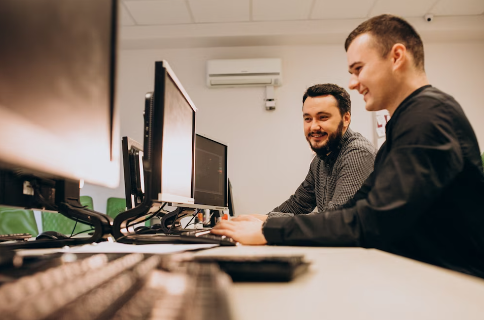 two men looking at the computer and smiling, one typing on the keyboard