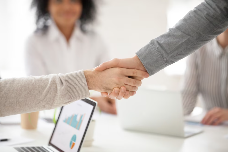 handshake, people at the desk, laptops on the blurred background