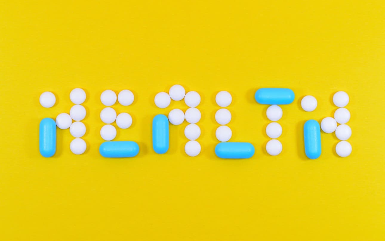 Pills arranged to spell HEALTH on a yellow background
