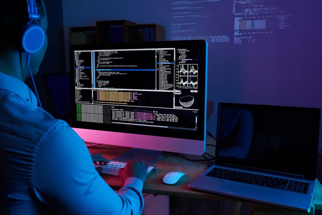 IT specialist checking code at computer in the dark office at night